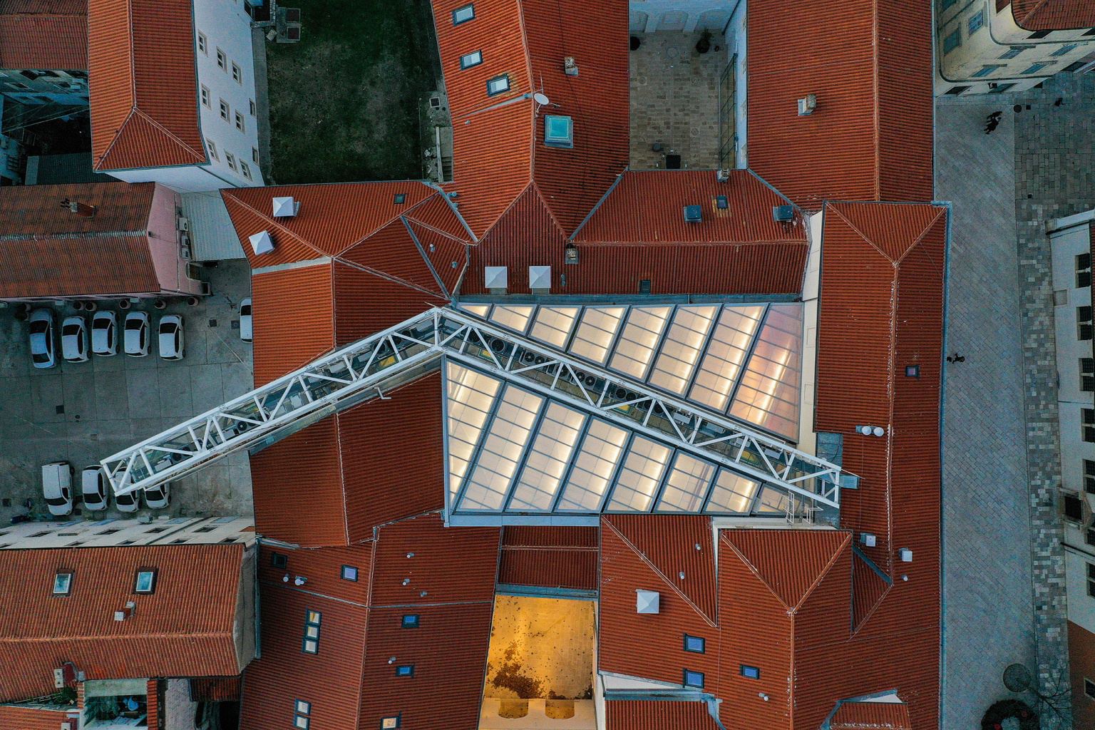 Aerial view straight down onto the terracotta roofs of II Palaces, a long glazed skylight running the length of the covered courtyard between them