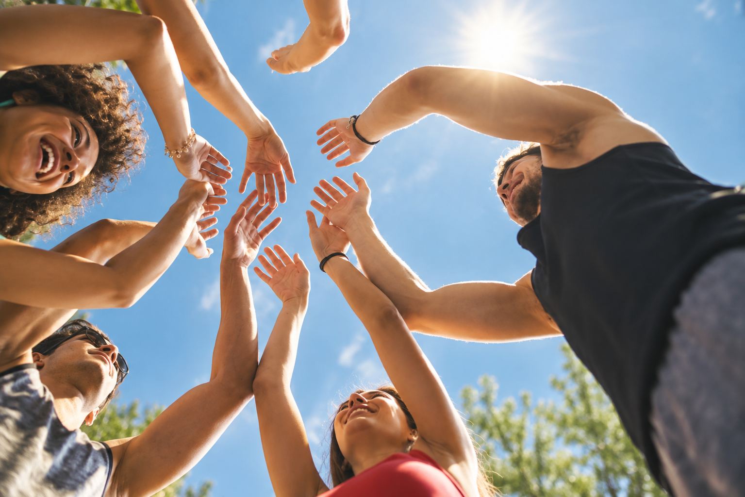 A circle of people seen from below, hands reaching towards each other against a bright blue sky